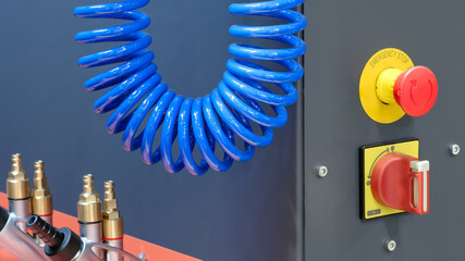 Poster - Industrial machine control panel with blue electrical wire twisted into a spiral, with a red emergency stop button and a rotary switch, industrial concept