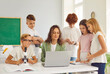 © Studio Romantic - School teacher and students learning, pupils around desk watching laptop in classroom. Female tutor and smart group gathering around table during lesson at school, watching educational video online