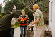 © Drobot Dean - A bald White woman in a colorful sweater laughs while dancing with diverse friends in a backyard. A man in a beanie and a cardigan raises his arms joyfully near a wooden table with wine and food.