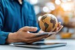 © artchvit - Global economy economic growth exports A person holds a globe above a tablet in a bright environment.
