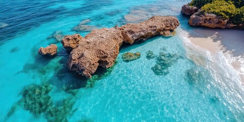 Aufkleber - Aerial view of a turquoise ocean with a rocky outcrop and sandy beach illuminated by sunlight reflecting on the water surface