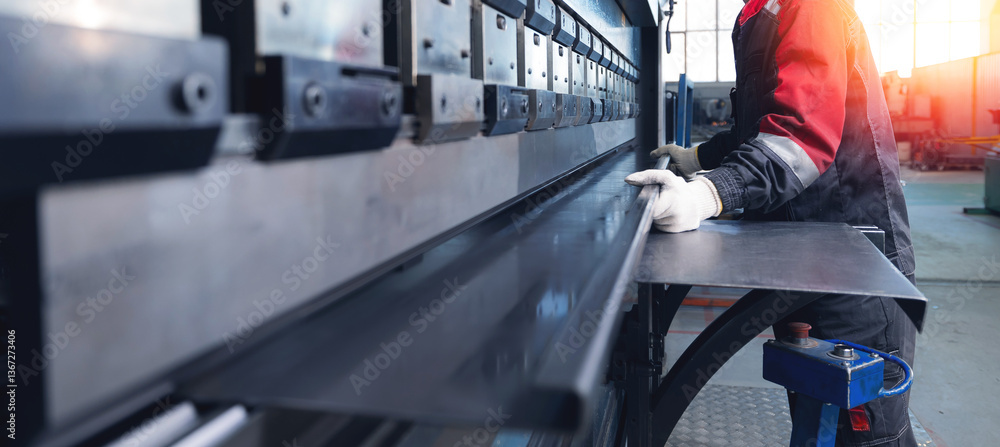 Male worker operating industrial metal press brake in factory setting ...
