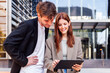 © Raul Mellado - man and a woman standing outside in front of office building, the man is pointing at digital tablet in the woman hand, concept of business and technology