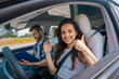 © Nataliya - Smiling young woman with license showing thumbs up and driving school instructor with clipboard in car. Driving test, driver courses, exam concept