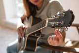 A talented young female musician is sitting alone and tuning a guitar. The lady plays a calm melody on a musical instrument.Music and hobbies.