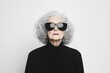 © VICHIZH - Mature woman exuding confidence in oversized black sunglasses and a stylish black coat, radiating elegance and individuality against a minimal white background