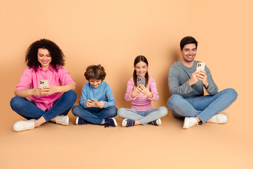 Happy family using smartphones together while seated on a beige background in casual attire, showcasing modern bonding