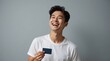 © Natsumae - Joyful young man, beaming with happiness, holds a blank card against a neutral gray backdrop. His radiant smile and positive expression convey pure delight and excitement.