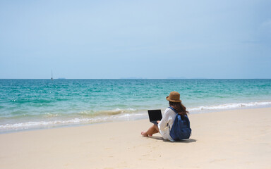Wall Mural - a female traveler using and working on laptop computer while sitting on the beach