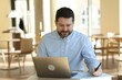 © New Africa - Handsome business owner working with laptop at table in his cafe