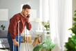 © Studio Romantic - Injured man posing on crutches after physical injury, has problem with mobility, making call via smartphone, being at home, has broken leg, trying to walk by himself, making good progress