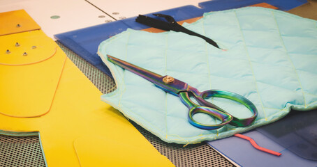 Leinwandbilder - A pair of scissors are lying on a blue blanket. The scissors are metal and have a rainbow handle. Concept of cutting and sewing clothes