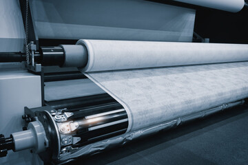 Aufkleber - A machine is rolling out a white fabric. The machine is in a factory. The fabric is being made in a factory