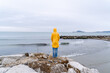© Bohdan - Young woman in yellow raincoat standing alone by the sea on a rainy day