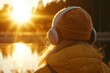 © serdon - The girl is standing on the pier by the lake, wearing headphones to listen to music, and taking in the view of the sunset as part of an ASMR concept