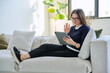 © Valerii Honcharuk - Middle aged woman sitting at home on sofa using digital tablet for video call, chat