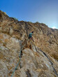© helivideo - BOTTOM UP: Female climber lead climbing up a high vertical rock wall. Using a rope and secured equipment, she ascends the challenging limestone surface, demonstrating strength and technical skill.