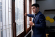 © Freeday photo - Professional man in a blue suit drinking coffee while looking out the window in a modern office setting during the afternoon