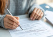 © Easy - Individual is filling out a personal information form at a desk, showcasing fingers holding a pen and papers scattered nearby in a relaxed indoor environment