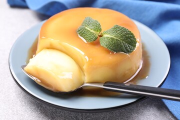 Wall Mural - delicious pudding with caramel sauce, mint and spoon on grey textured table, closeup