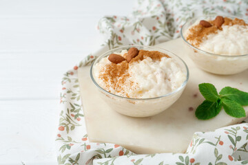 Wall Mural - delicious rice pudding with cinnamon, almonds and mint on white wooden table, closeup. space for tex