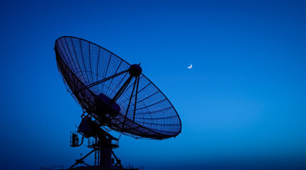 Wall Mural - large satellite dish silhouetted against a twilight blue sky