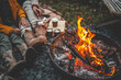 © shine.graphics - Family or friends relaxing by a campfire, roasting marshmallows on sticks. Boots, cozy clothes, hot drinks, and warm flames create a peaceful outdoor autumn evening vibe