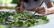 © David Giraud - Une femme dessinant une maquette architecturale d'une ville, avec des espaces verts, des bâtiments et des éoliennes, concept de construction pour un développement urbain durable.