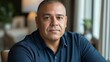 © Lisouski Uladzimir - Confident middle-aged hispanic man in blue shirt near window in natural light