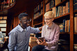 © Marko Geber - Diverse student friends using smartphone and laughing together in library