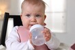 © New Africa - Cute little baby with bottle on feeding chair at home