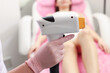 © New Africa - Professional cosmetologist holding laser depilator near patient in beauty salon, closeup