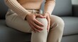 © rdkcho - Woman Experiencing Knee Pain While Sitting on a Sofa, Close-up View