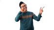 © Jamaludinyusup - A friendly Asian Muslim man making a 'call me' hand gesture while pointing to the right at empty copy space, looking at the camera with an inviting expression. Isolated on a white background