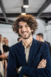 © Davide Zanin - Smiling young businessman working inside modern office with the multiethnic team behind him - Concept of leadership and achieving goals - Focus on eyes - Vertical editing