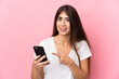 © luismolinero - Young caucasian woman isolated on pink background using mobile phone and pointing it