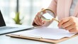 © dreamer - A person examines documents with a magnifying glass, highlighting attention to detail in a professional environment.