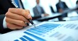 © David Giraud - Un homme d'affaires tenant un stylo dans sa main, vue en gros plan, consultant des graphiques et tableaux d'analyses financières dans une réunion de travail.