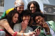 © Ladanifer - Group of cheerful multi ethnic young activists wearing rainbow bracelets and watching something funny on a smartphone during LGBT pride parade