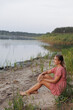 © Anhelina  - A woman in a red dress sits barefoot on the lakeshore, surrounded by wild nature. She smiles and enjoys the tranquility, creating an atmosphere of harmony, relaxation, and connection with nature