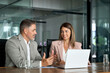 © insta_photos - Two busy middle aged colleagues company board discussing digital strategy at corporate meeting. Professional business executive managers office team working using laptop computer sitting at table.