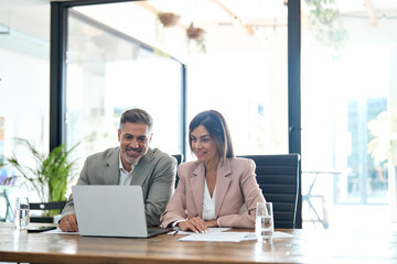 Fototapete - Two happy professional business partners wearing suits working in office looking at computer technology, executive leaders managers discussing digital strategy together at corporate meeting.
