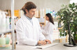 © JackF - Male pharmacist in uniform looking for medicine in pharmacy using computer. In the background, female pharmacist places medicine on shelves