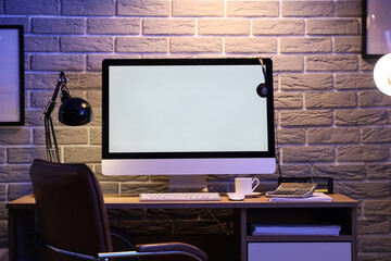 Blank computer monitor with glowing lamp on desk in office at night