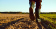 © Valua Vitaly - Low angle: man walking in rubber boots in a farmer's field, the blue sky above the horizon. Man walking through an agricultural field. Farmer walks through a plowed field in early spring.