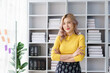 © Pichsakul - Smiling young businesswoman in yellow sweater standing confidently in bright and modern office space