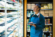 © unai - Saleswoman using digital tablet checking food products in refrigerator at organic supermarket