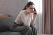 © New Africa - Depressed woman calling hotline for mental health help on sofa at home