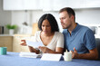 © Antonioguillem - Angry interracial couple reading bank statement in the kitchen