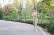 © Jirawatfoto - Asian woman jogging on peaceful park pathway surrounded by lush greenery, wearing light athletic wear and expressing calm and focused demeanor. Healthy and active lifestyle concept